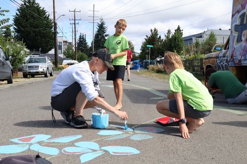Three kids paining flowers on a street for the NE Greenwood Home Zone mural.